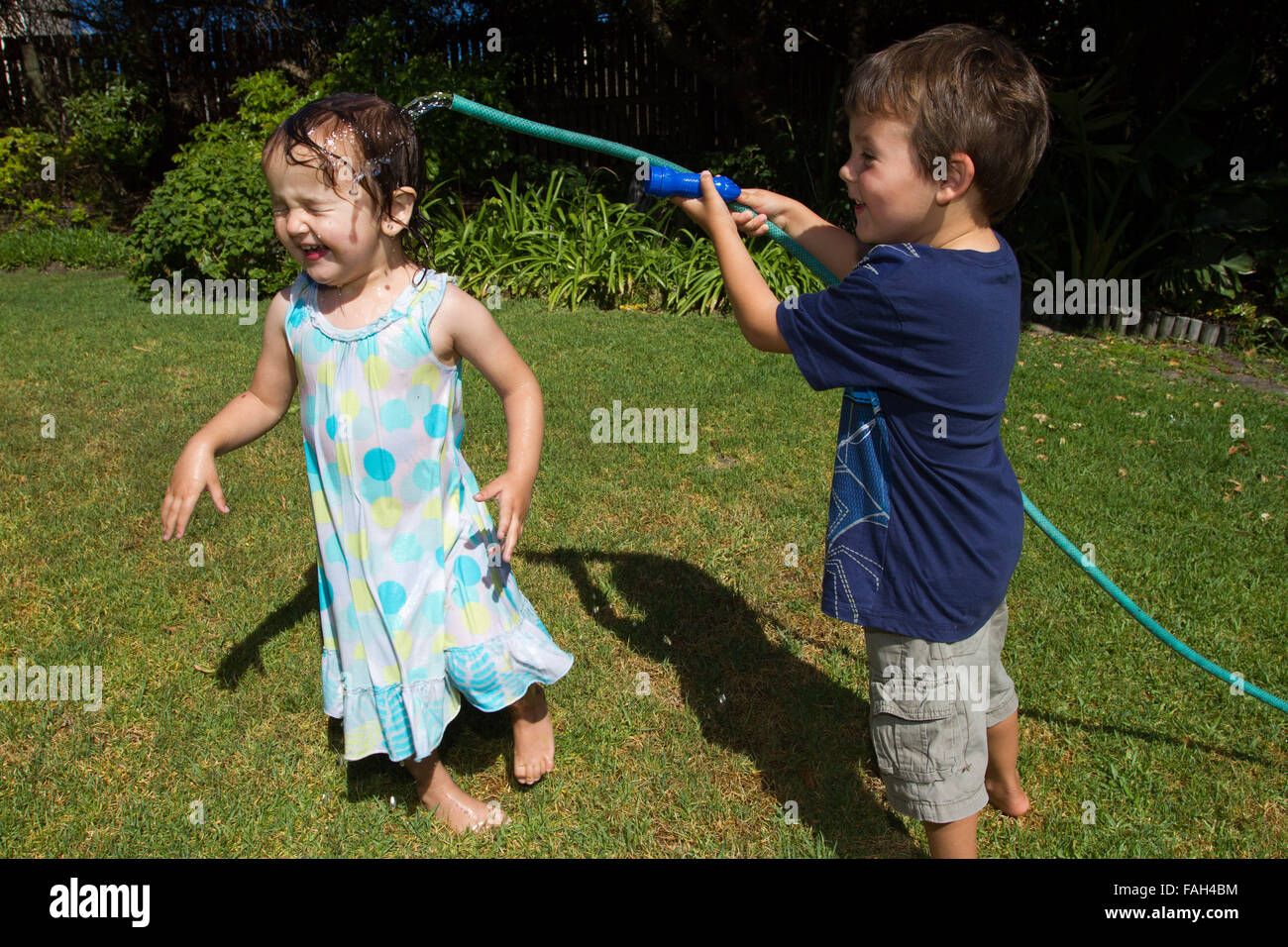 Little boy hosing down his little sister in the garden. Stock Photo
