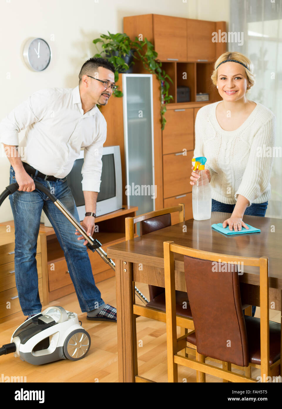Cheerful husband helping his wife cleaning the room. Focus on woman ...