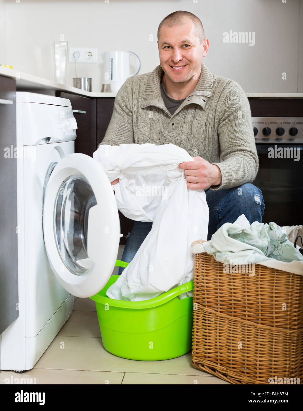 Home laundry. Smiling man using washing machine in kitchen at home Stock Photo