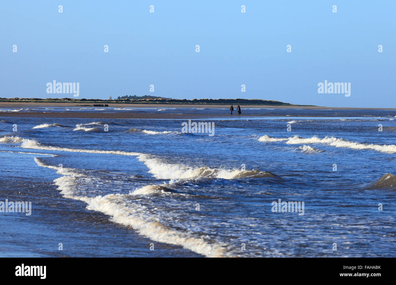 Two women walking with a dog and Brancaster beach on a sunny Winter's day. Stock Photo