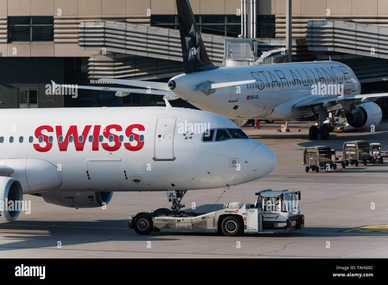 An aircraft tug is pushing an Airbus A320 of Swiss International Air Lines away from the gate at Zurich international airport. Stock Photo