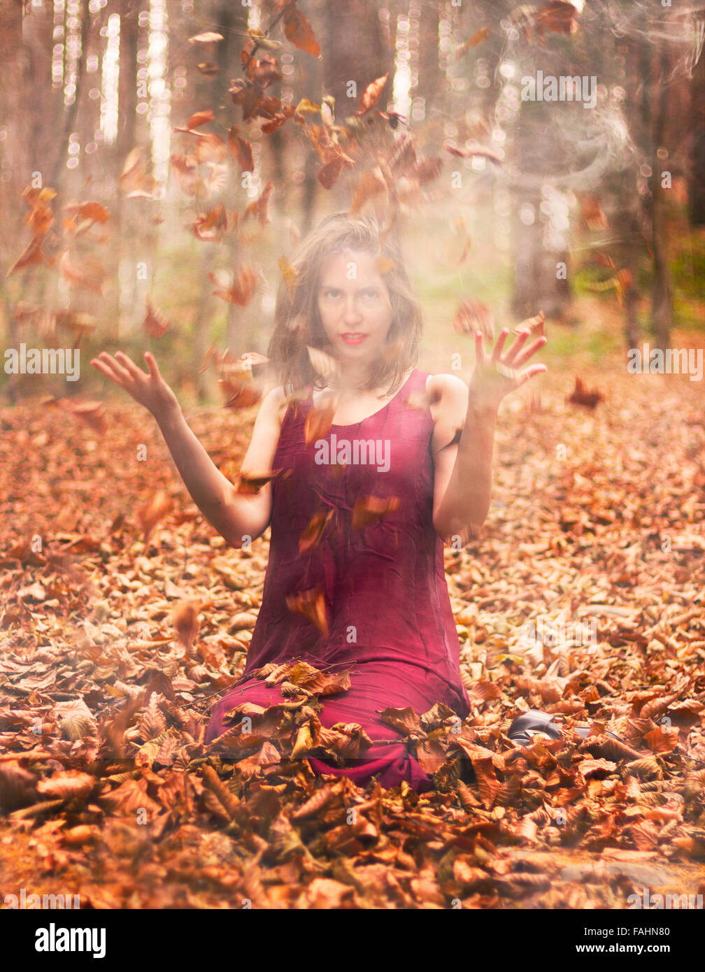 Women in burgundy dress throwing leaves up in the air, surrounded by smoke Stock Photo