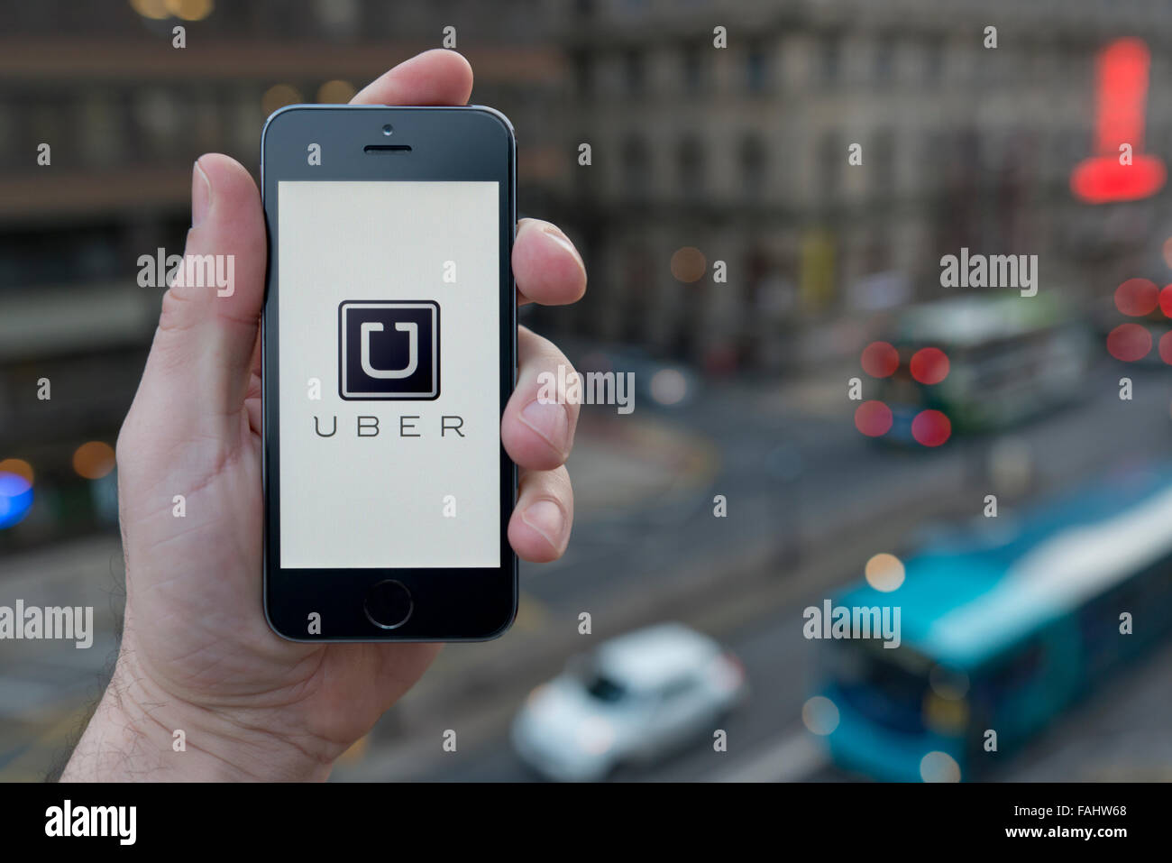 A man uses the Uber taxi smartphone app while stood in a tall building overlooking a busy city street (Editorial use only) Stock Photo