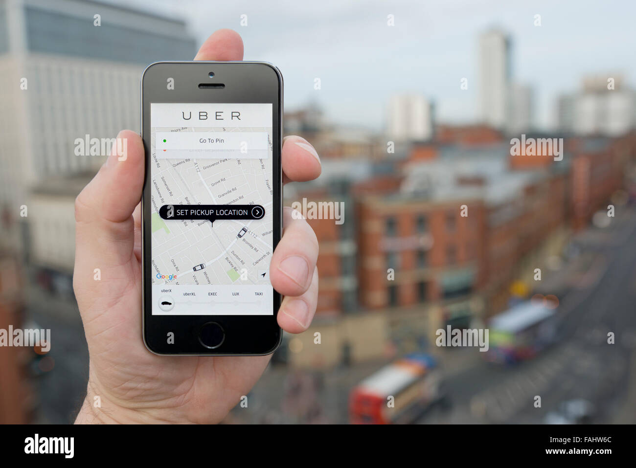 A man uses the Uber taxi smartphone app while stood in a tall building overlooking a busy city street (Editorial use only) Stock Photo