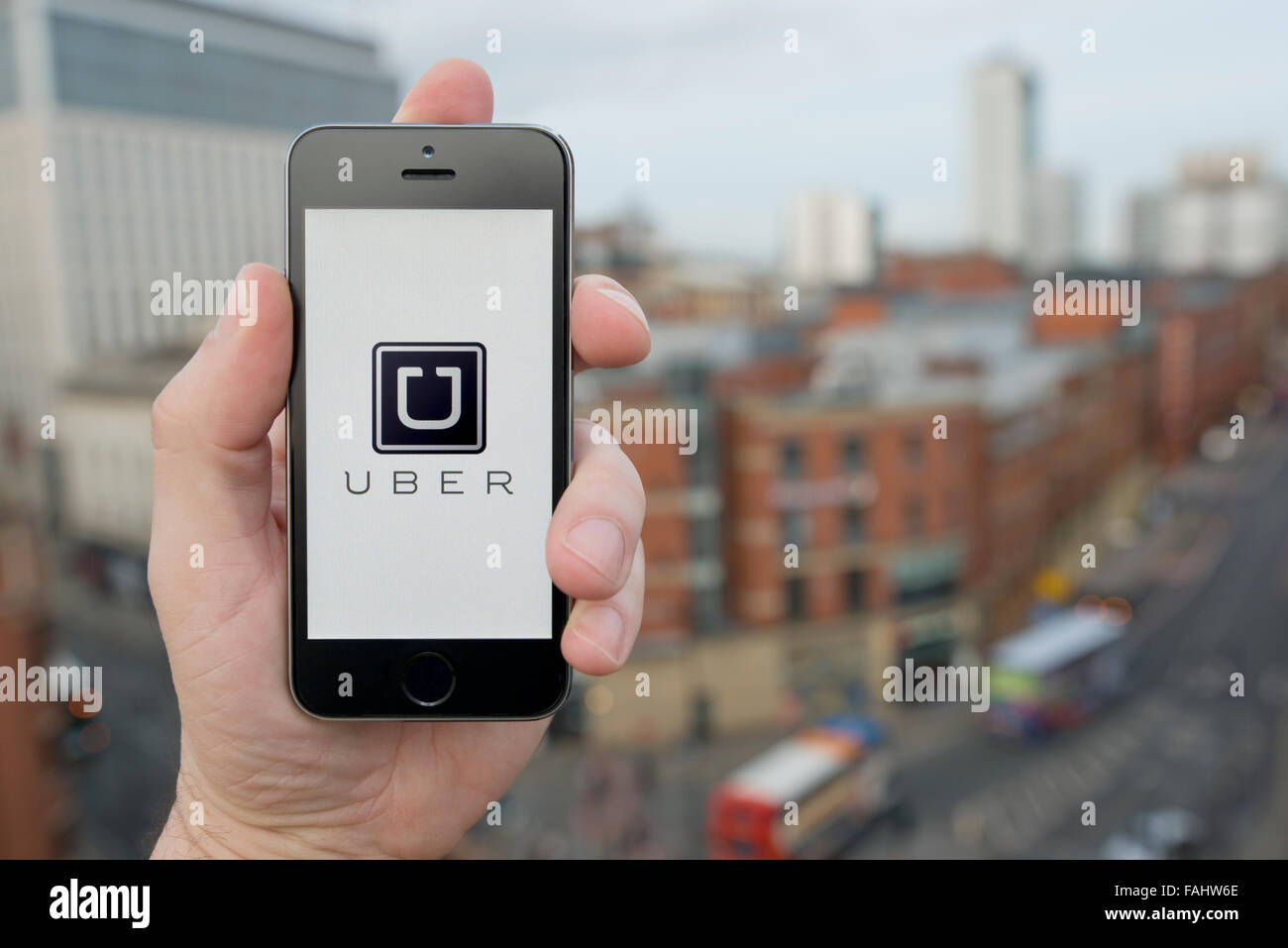 A man uses the Uber taxi smartphone app while stood in a tall building overlooking a busy city street (Editorial use only) Stock Photo