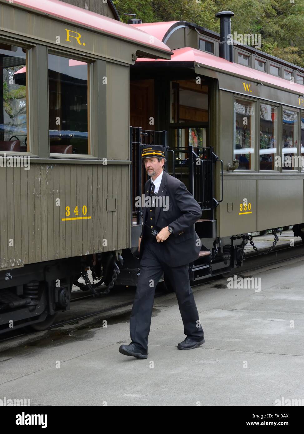 Passenger transportation train carriages and conductor in uniform at the harbour in Skagway, Alaska, USA Stock Photo