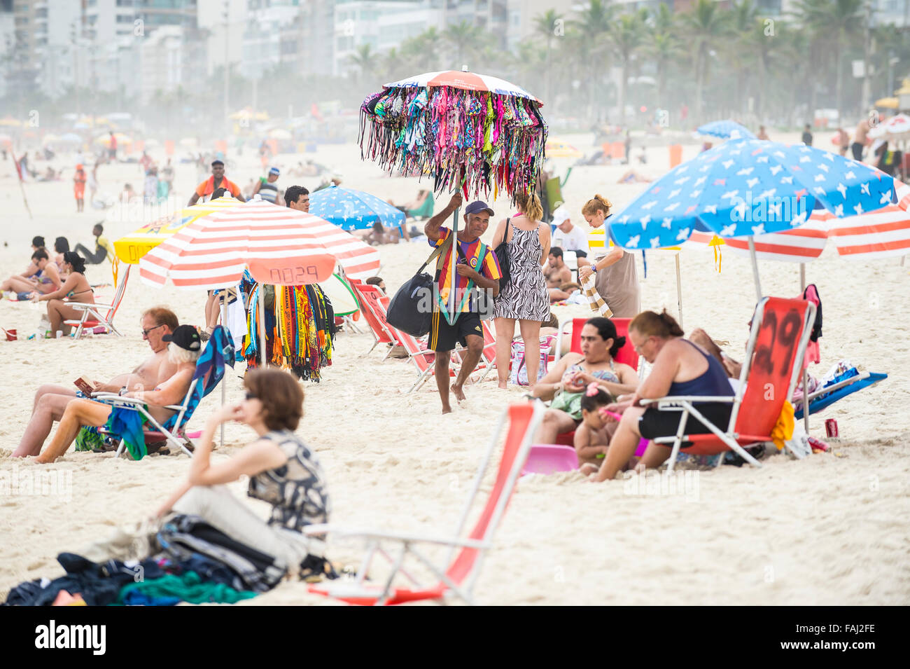 RIO DE JANEIRO, BRAZIL - OCTOBER 27, 2015: Beach vendor selling bikinis walks with his merchandise hanging from a beach umbrella Stock Photo
