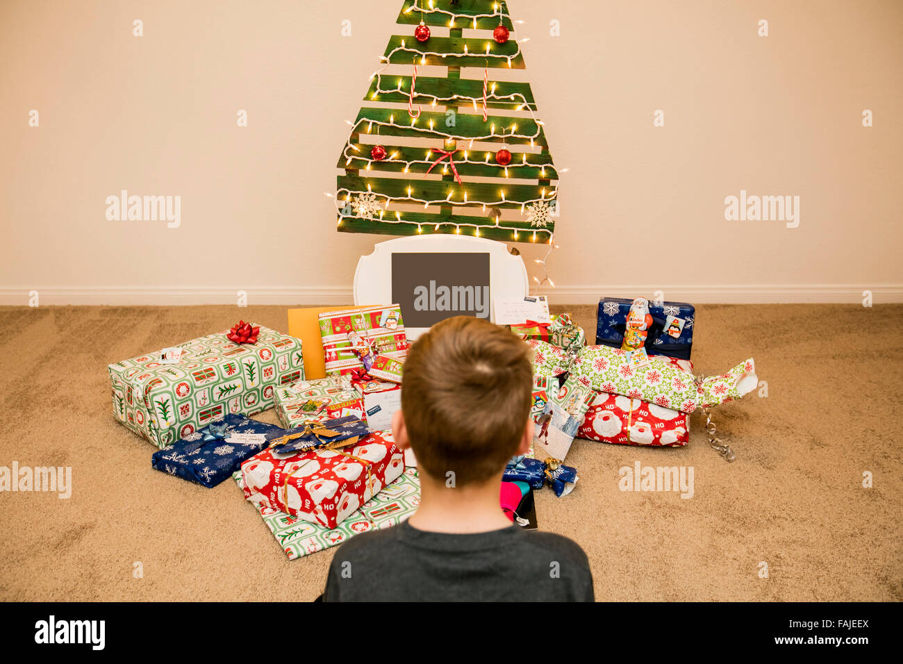 young boy looks at the Christmas presents under an ecological reusable Christmas tree