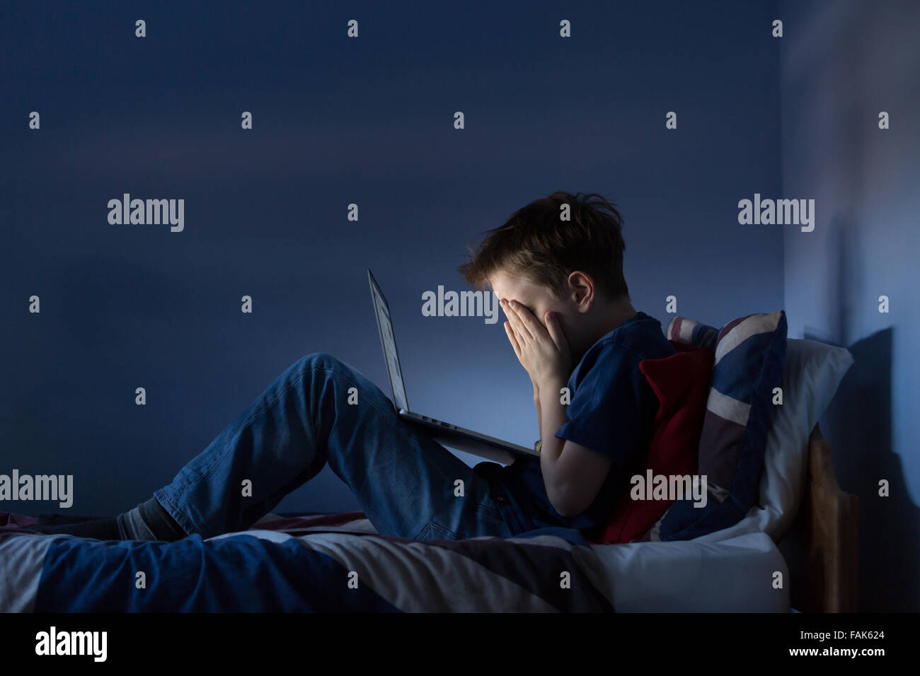 Online bullying Cyber bullying photo of an upset boy in his bedroom looking at hurtful messages on social media Stock Photo