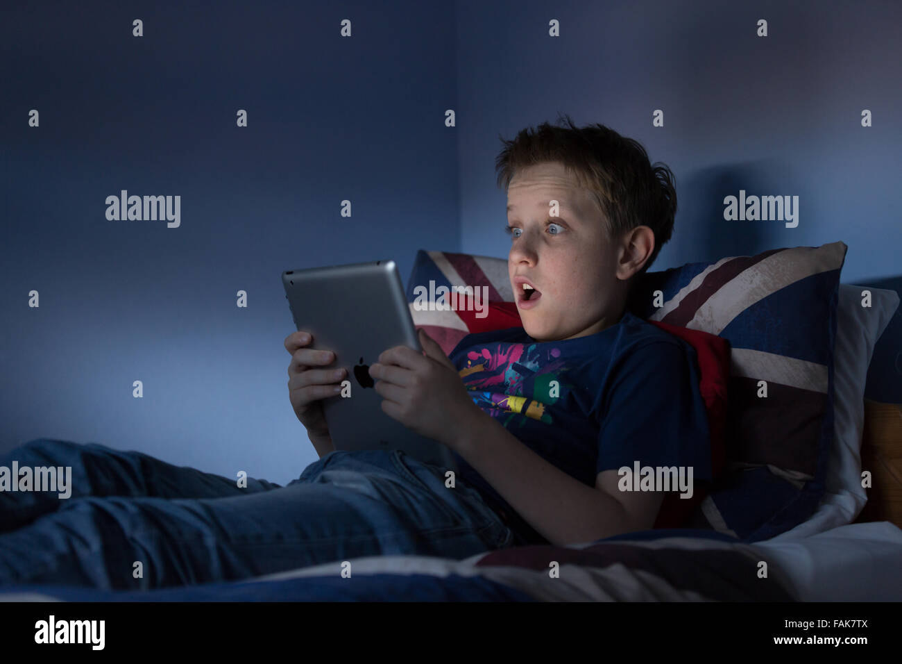A boy sitting up late in his bedroom looking at the internet shocked at what he is seeing Stock Photo