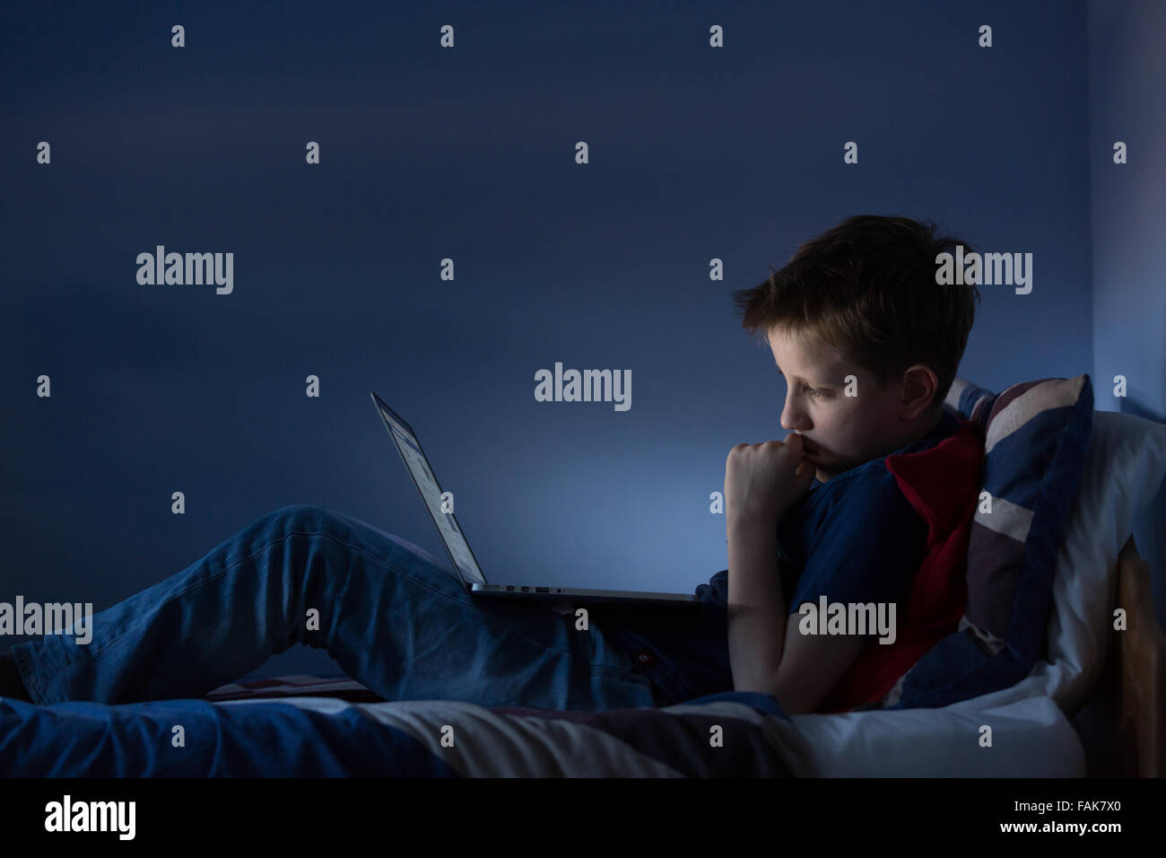 Online bullying Cyber bullying photo of an upset boy in his bedroom looking at hurtful messages on social media Stock Photo