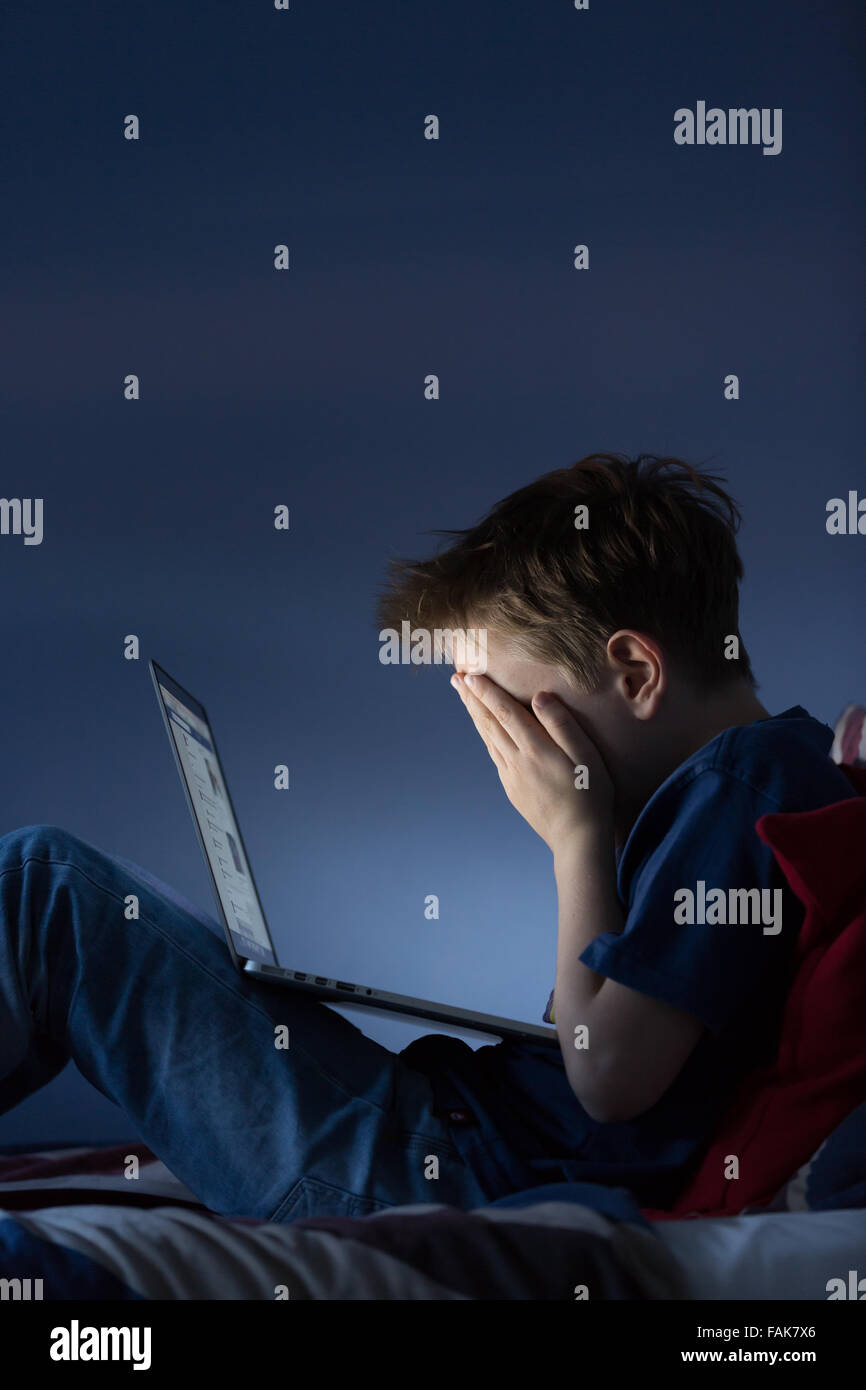 Online bullying Cyber bullying photo of an upset boy in his bedroom looking at messages on social media Stock Photo