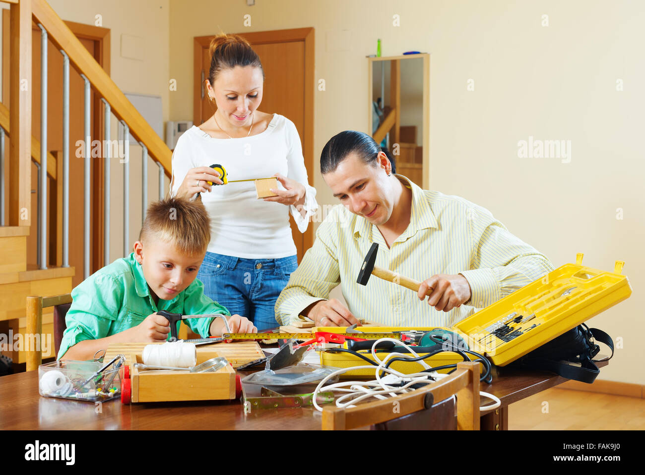 Father and son are doing with their hands crafts in home, woman helps them Stock Photo