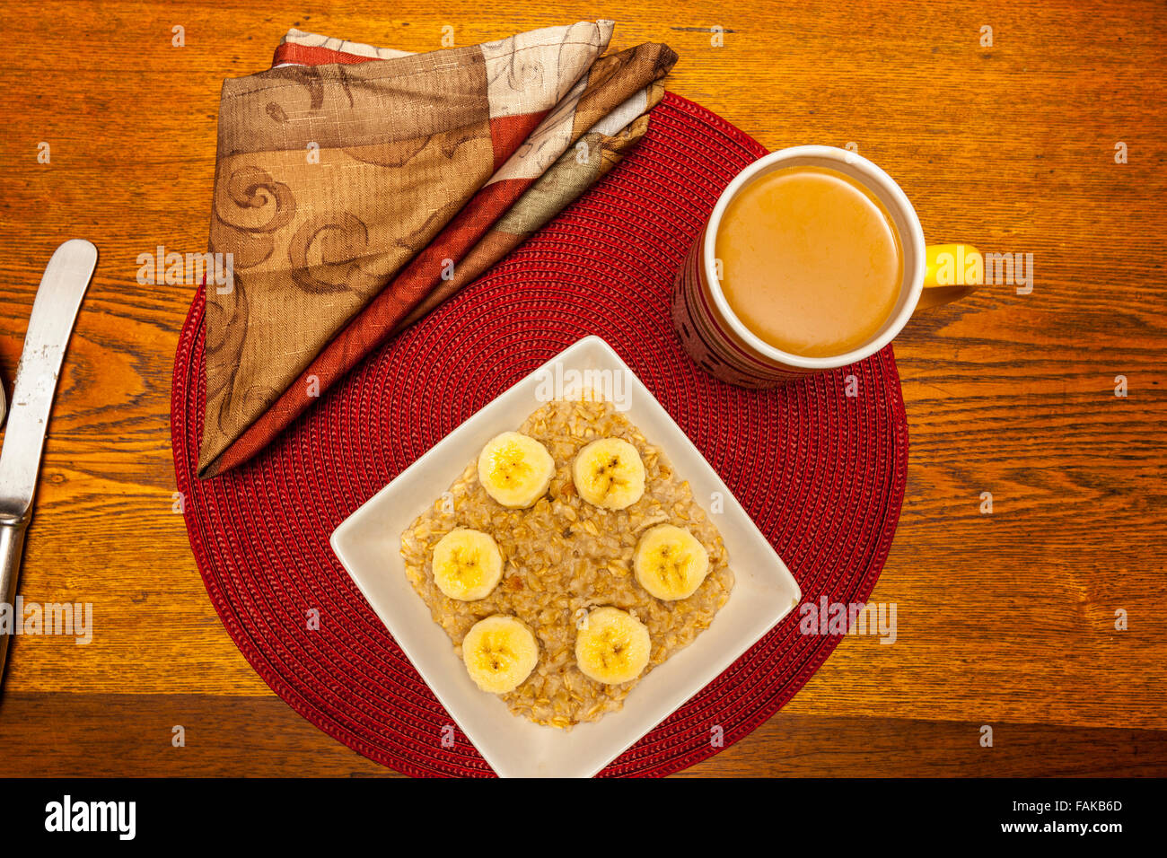 A bowl of oatmeal with banana slices and cinnamon on a round placemat on a wooden table Stock Photo