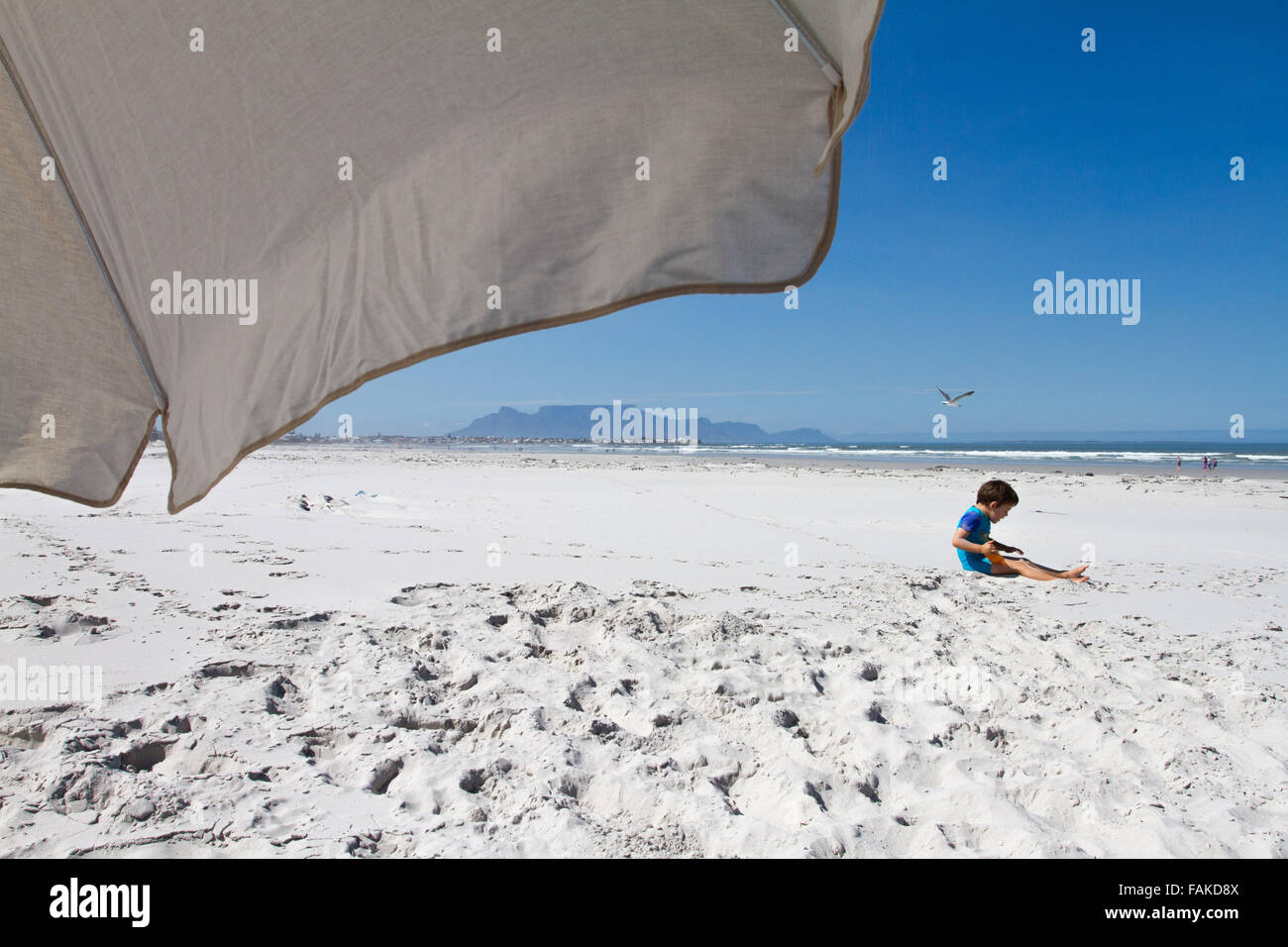 Little boy on the beach at Melkbosstrand, with Table Mountain in the background Stock Photo