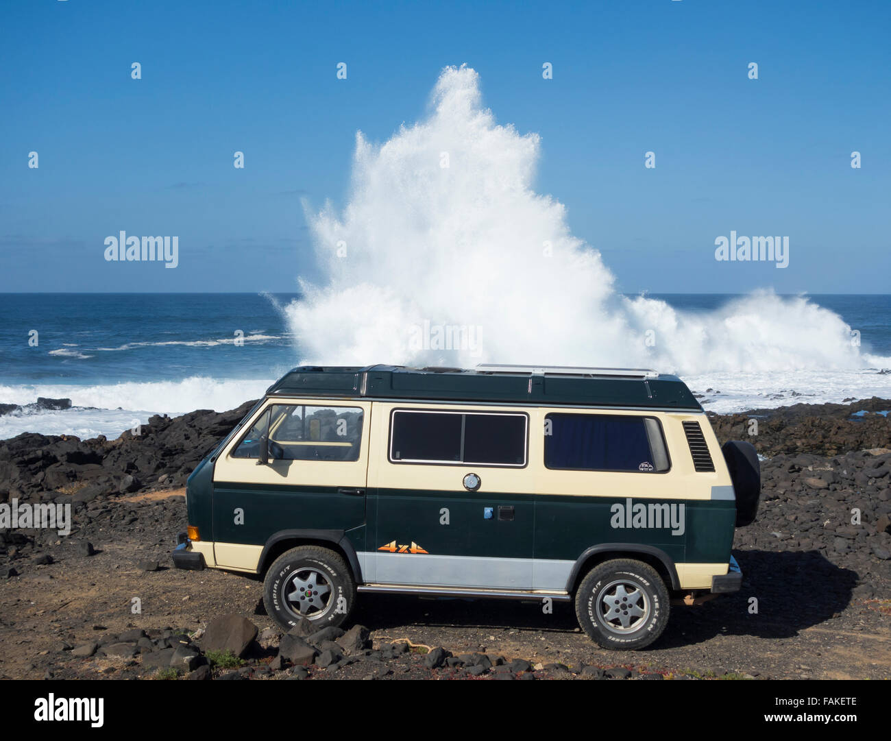 4x4 VW camper van with solar panel on roof parked on rocky surfing beach with huge waves breaking. Gran Canaria, Canary Islands. Stock Photo