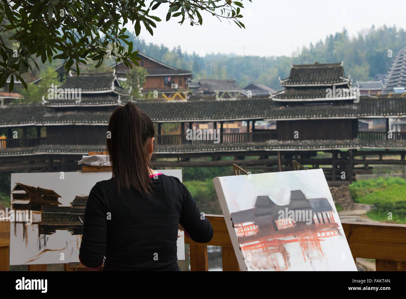 Girl painting by Dong styled Wind-An-Rain bridge, Chengyang Scenic Area, Sanjiang, Guangxi Province, China Stock Photo