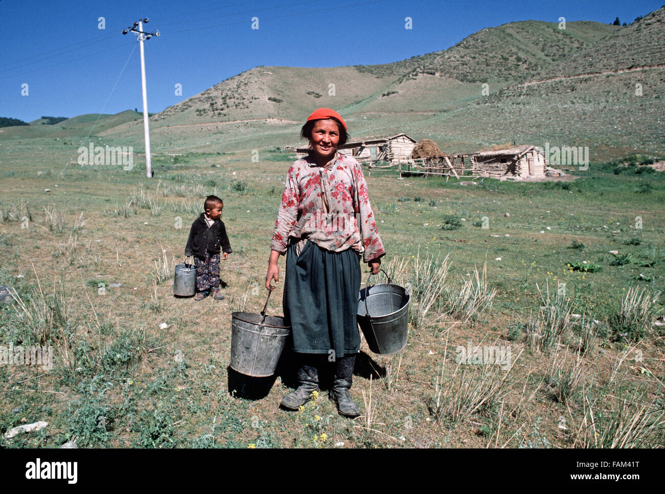 Kazakh mother and son carrying water buckets from farmhouse in hills North of Urumqi, Xinjiang Province, China Stock Photo