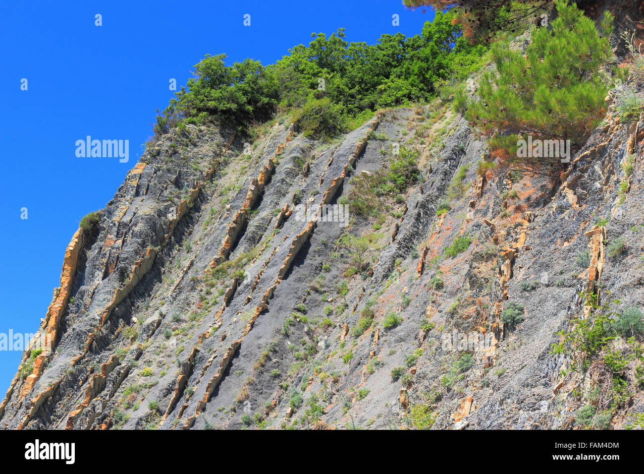 Steep slopes with sparse vegetation and visible layers of rock Stock Photo