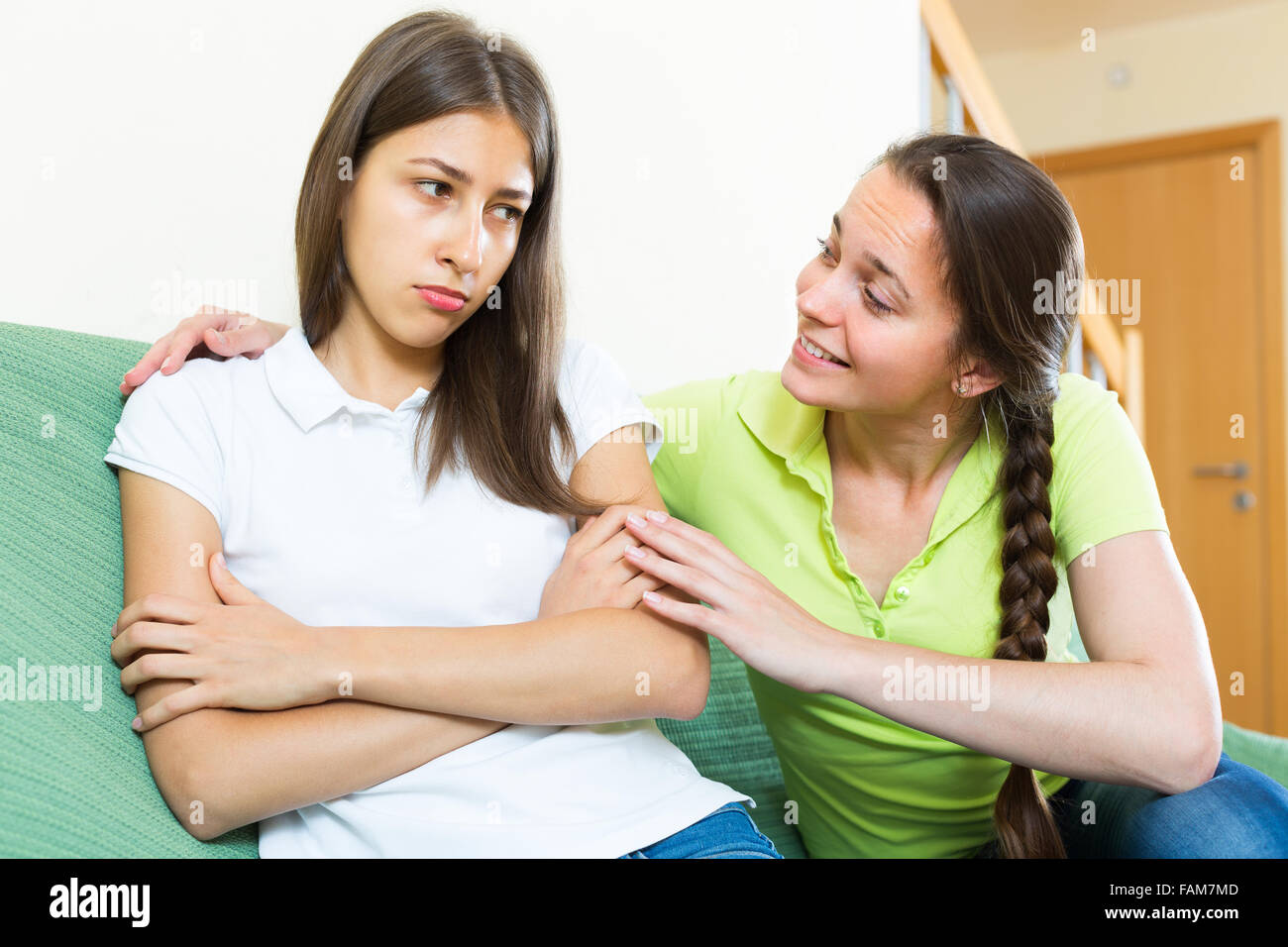 Smiling longhaired girl comforting her sad teenage sister at home Stock Photo