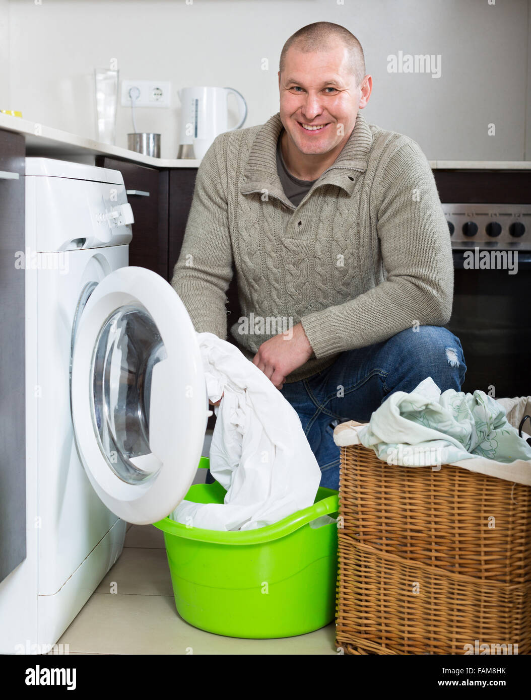 Home laundry. Smiling guy using washing machine in kitchen at home