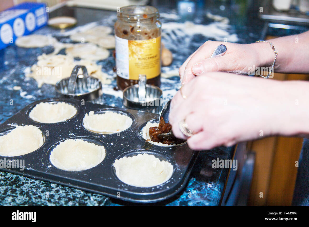 Making mince pies adding mincemeat to pastry cases cooking in kitchen baking tray Stock Photo