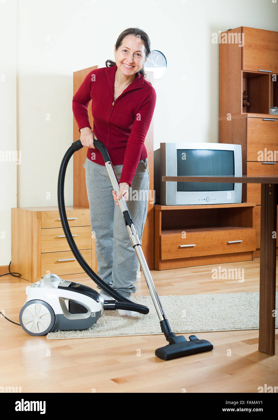 Happy mature woman cleaning with vacuum cleaner Stock Photo