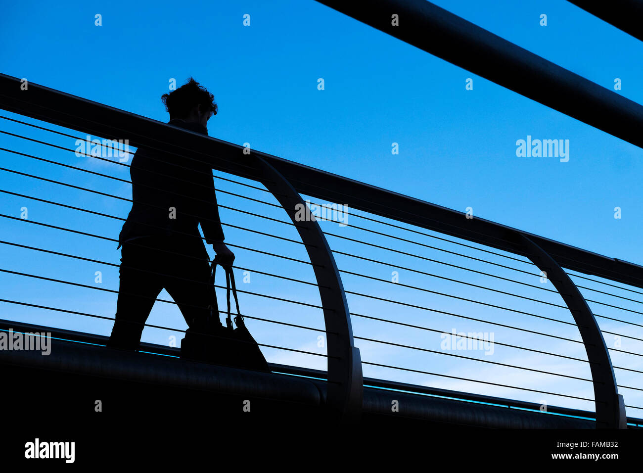 A woman seen in silhouette as she walks across the Millenium Bridge in London. Stock Photo