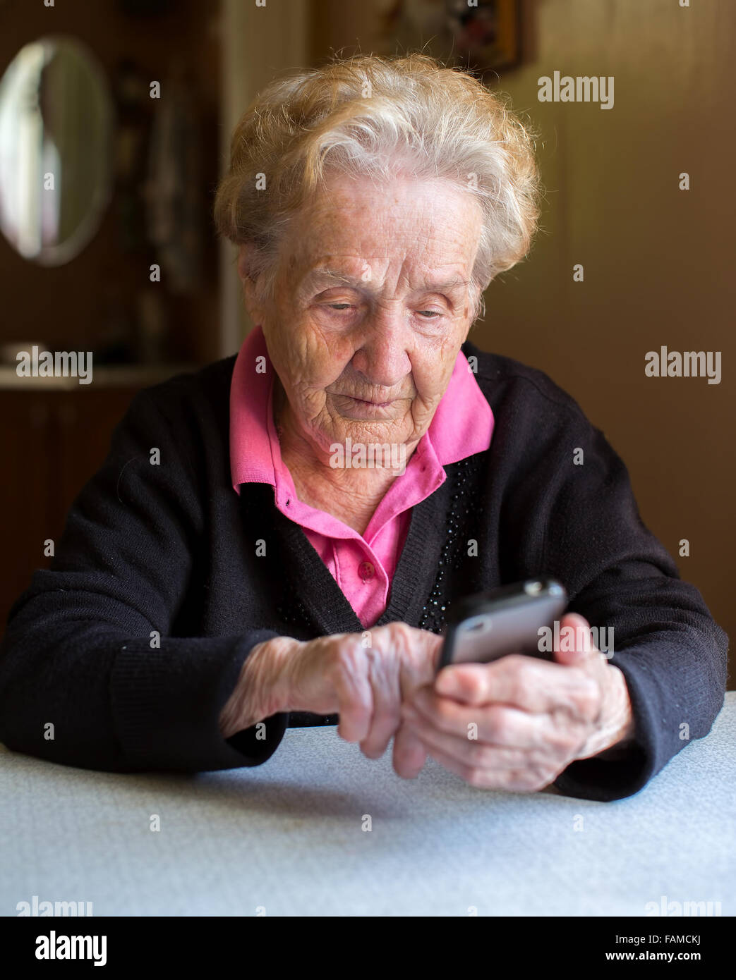 An elderly woman typing on smartphone sitting at the table. Stock Photo