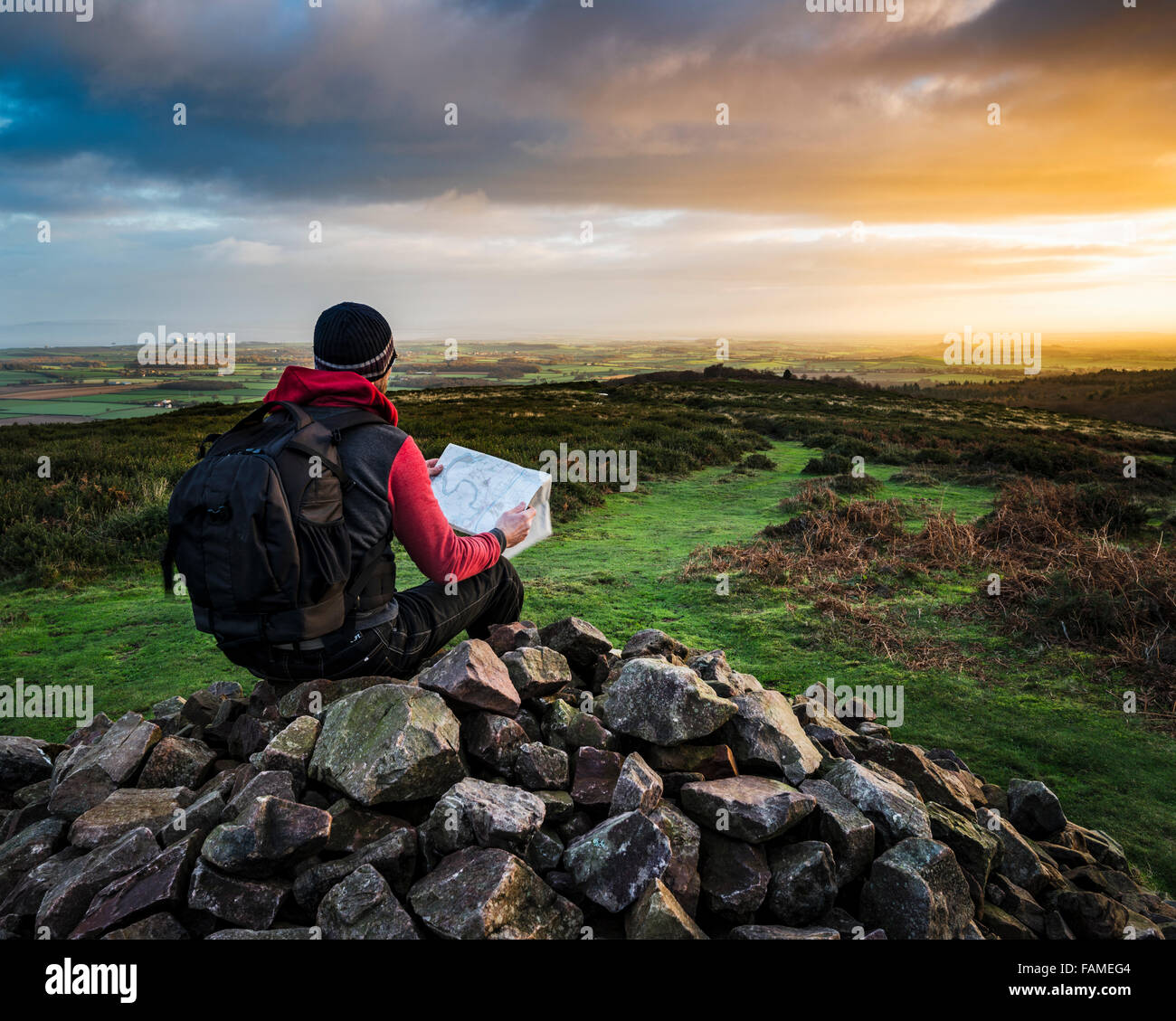 A walker sitting on top of a cairn, reading a map, at sunrise on the Quantock hills, Somerset, UK Stock Photo