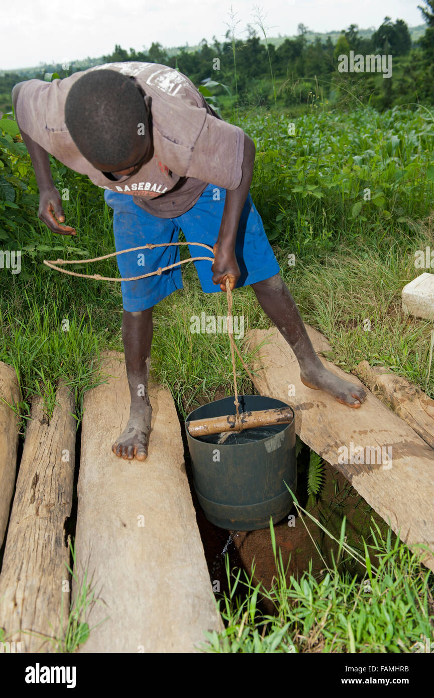 Child drawing water up from a deep well with bucket and rope ...