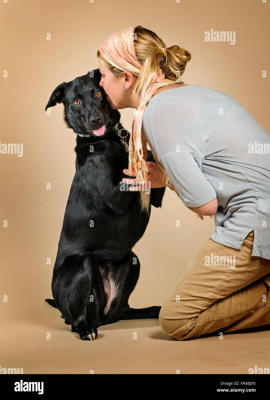 Studio portrait of attractive blonde Caucasian woman with her black laborador - collie mix breed dog Stock Photo