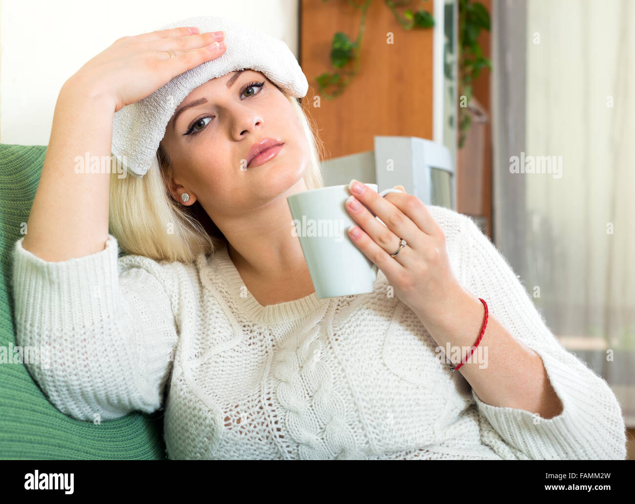 Feeling sick woman is sitting on a sofa at home with a wet cold towel