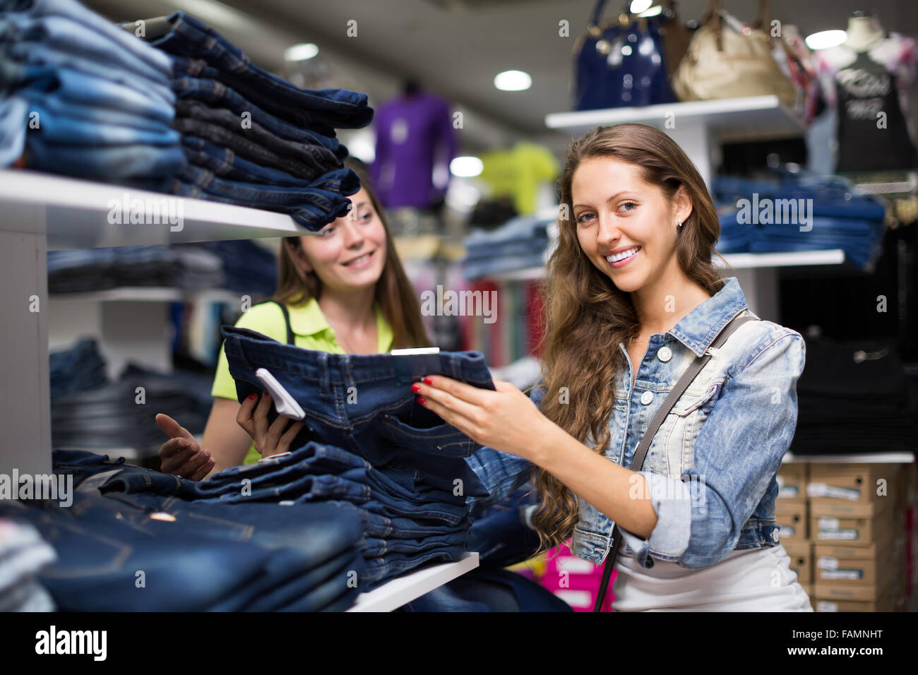 Smiling young longhaired woman choosing new jeans at store Stock Photo