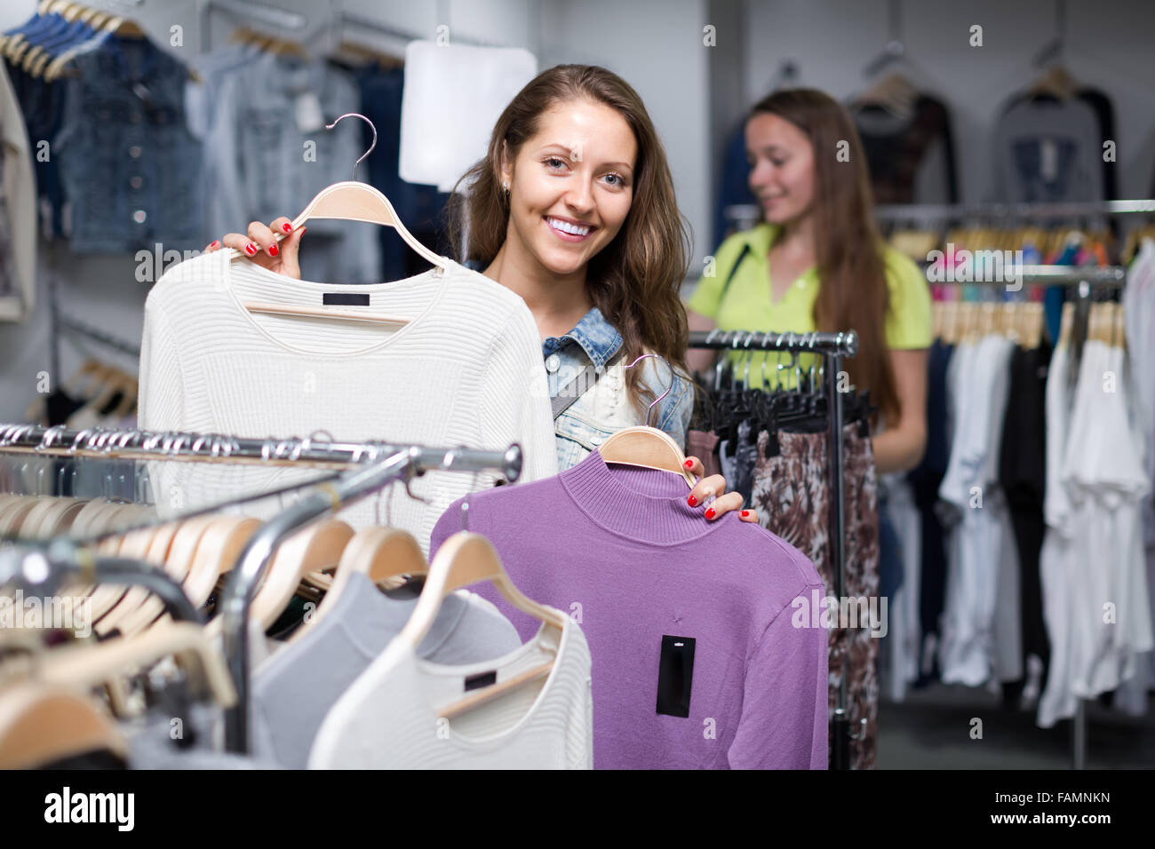Attractive smiling young longhaired girl choosing pullover in shop Stock Photo