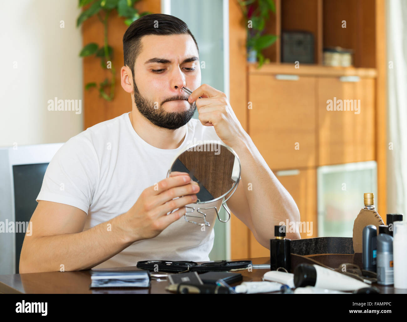 Young Guy Looking At Mirror And Removing Nose Hair With Tweezers