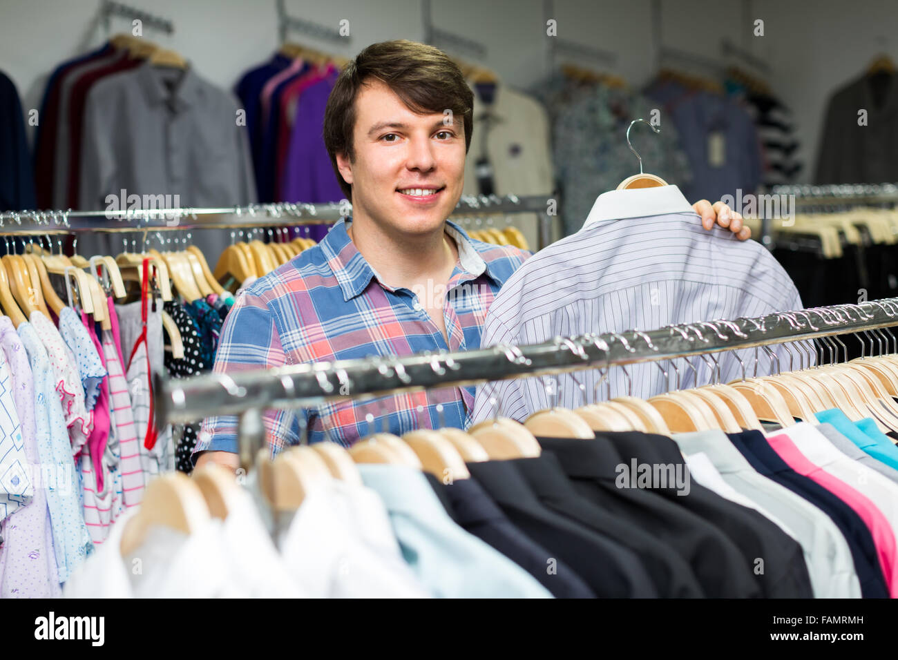 Young man choosing shirts at clothing store and smiling Stock Photo - Alamy