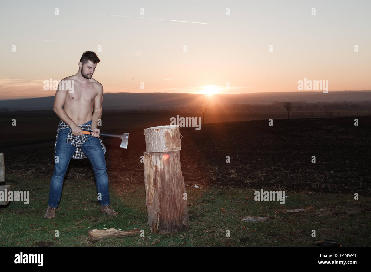 The stylish lumberjack chopping wood at sunset. Stock Photo