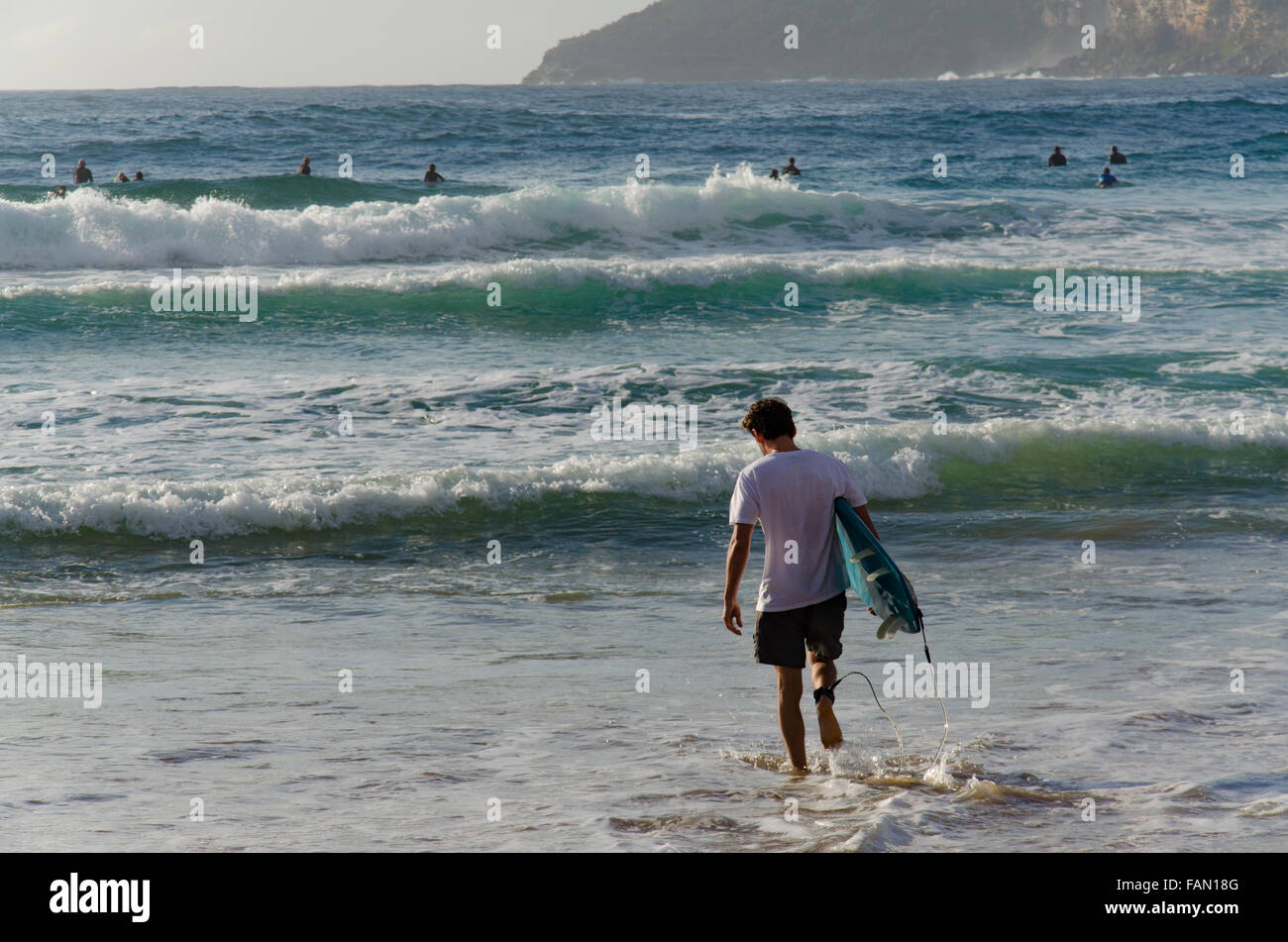 A surf board rider walks into the surf on a sunny morning at Freshwater Beach in Sydney Stock Photo