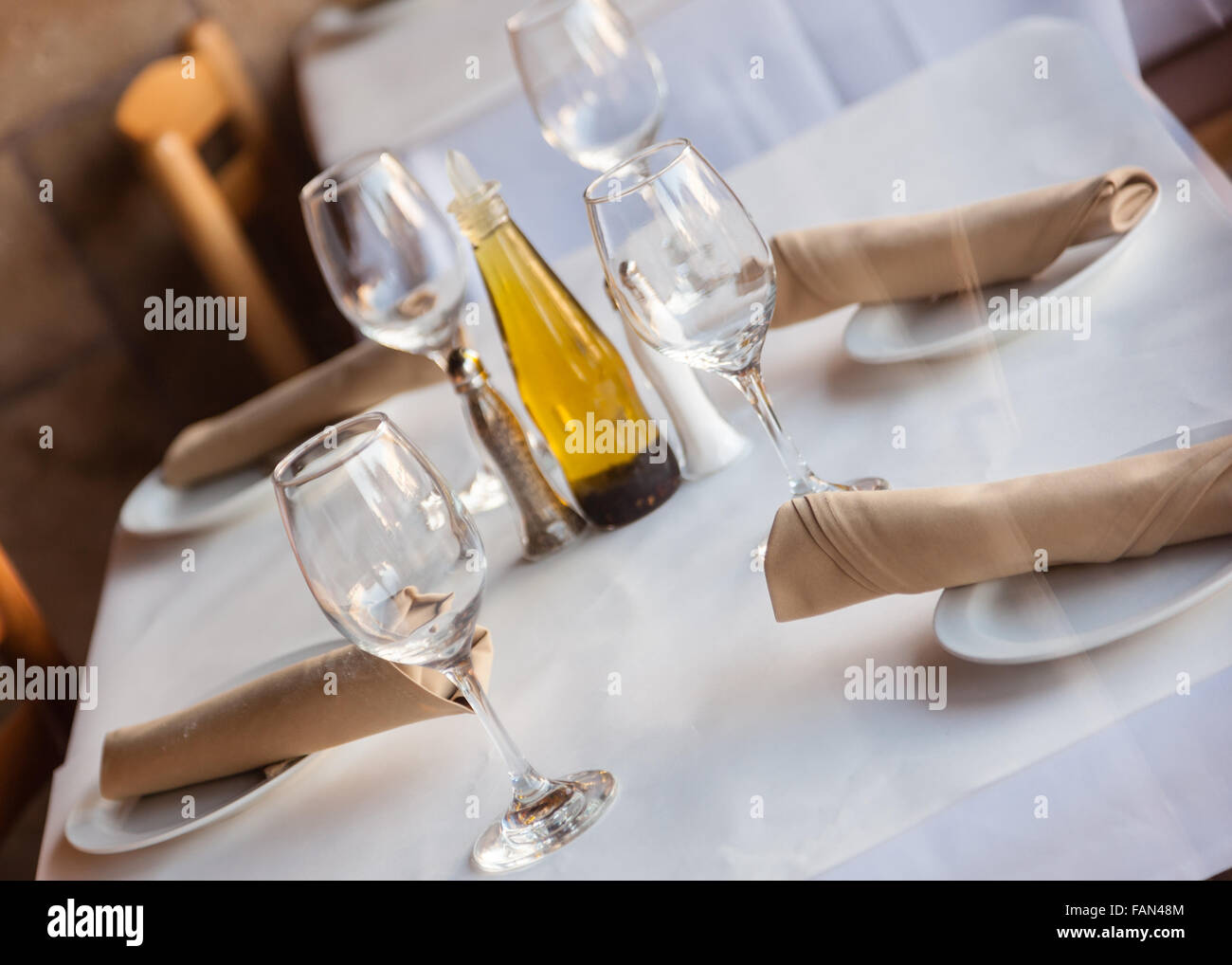 Simple Table setting in a restaurant with white tablecloth napkins and wine glasses. Stock Photo