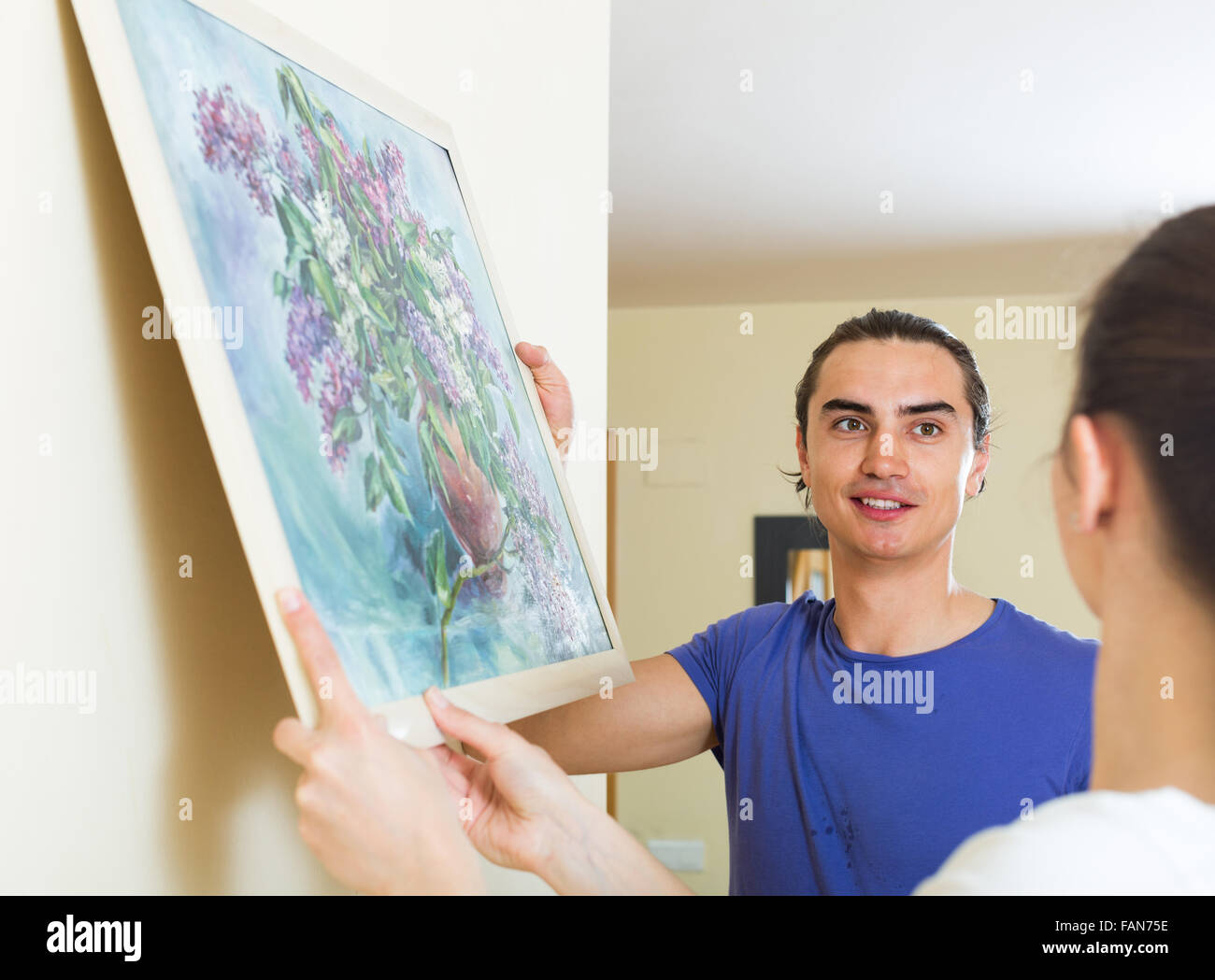 Positive married couple hanging picture in frame on the wall in living