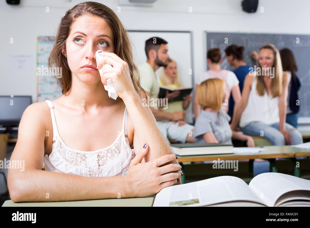 Sad crying girl sitting at her desk alone in college classroom Stock