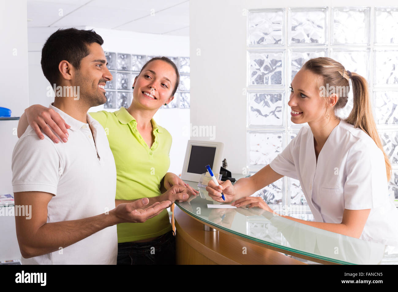 Positive young couple talking with smiling secretary at reception in the clinic Stock Photo