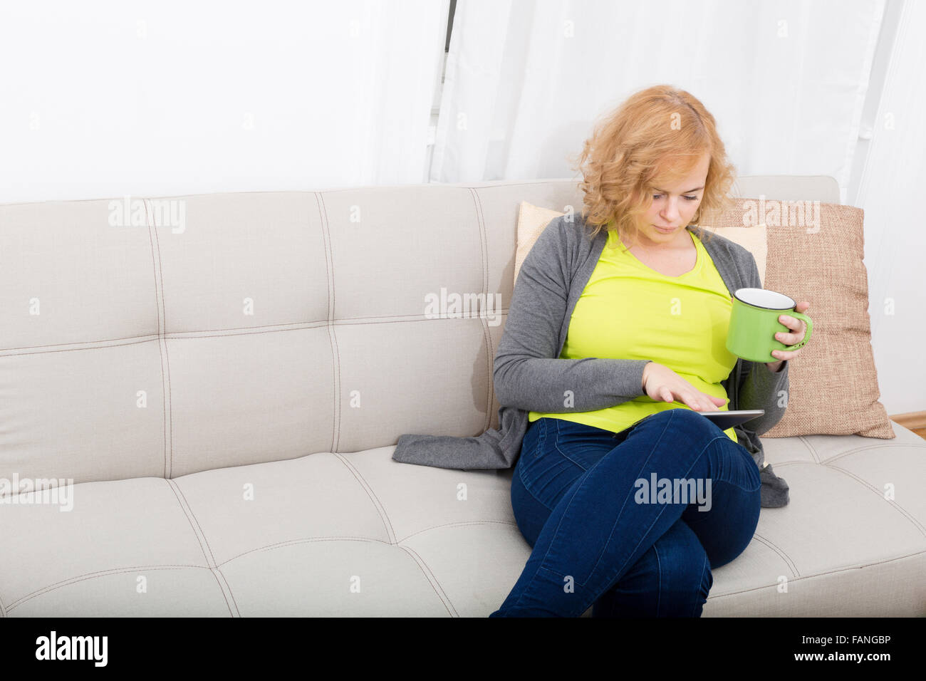 A Young Plus Size Woman With A Tablet Pc Sitting On A Sofa Stock