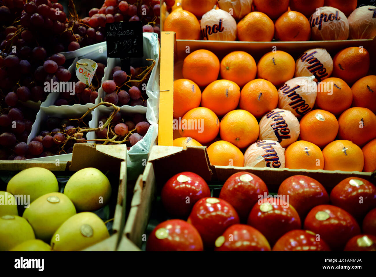 Apples, oranges and grapes for sale in a market stall in their crates
