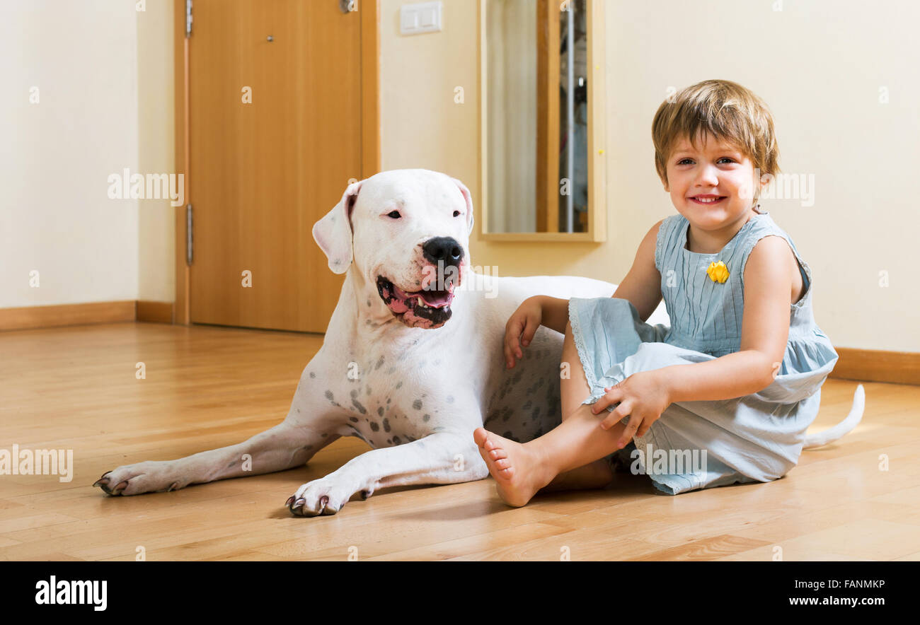Positive smiling little girl with big white dog sitting on the floor at ...