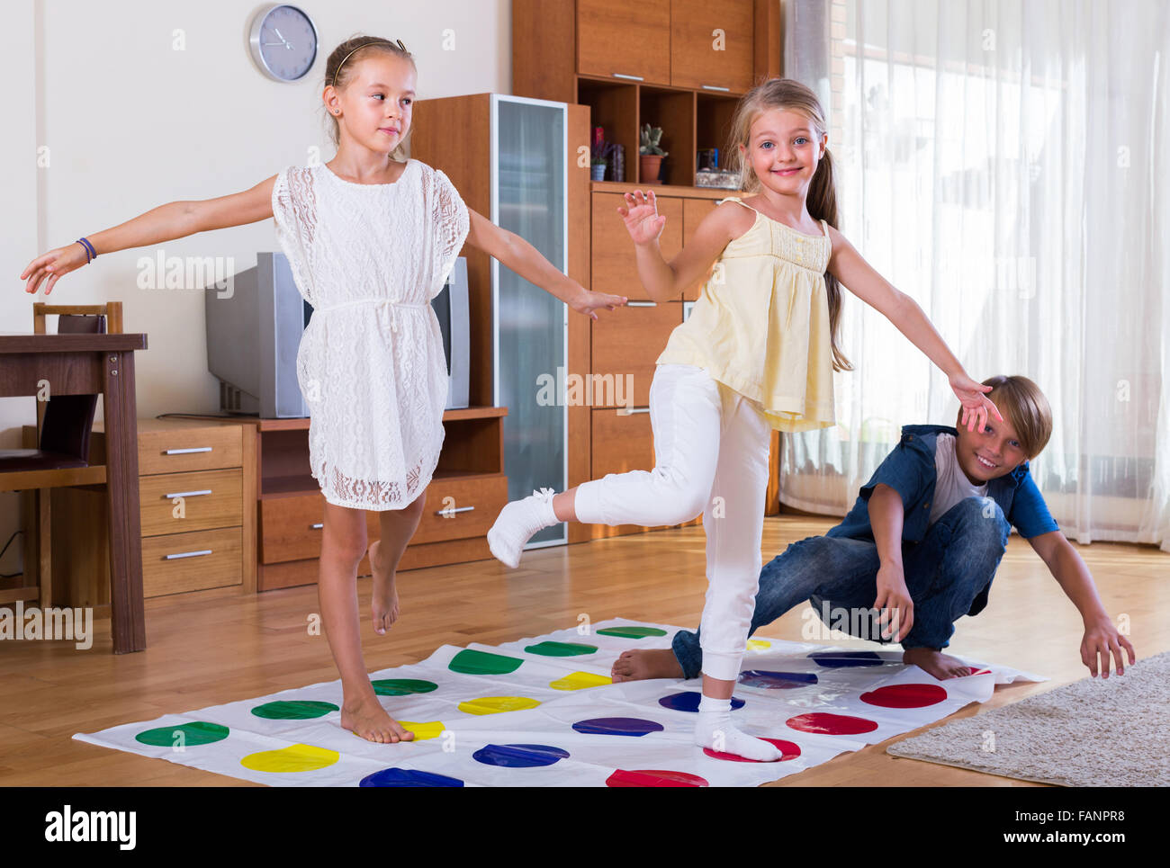 Two cute little girls and teenage boy playing twister at home Stock Photo