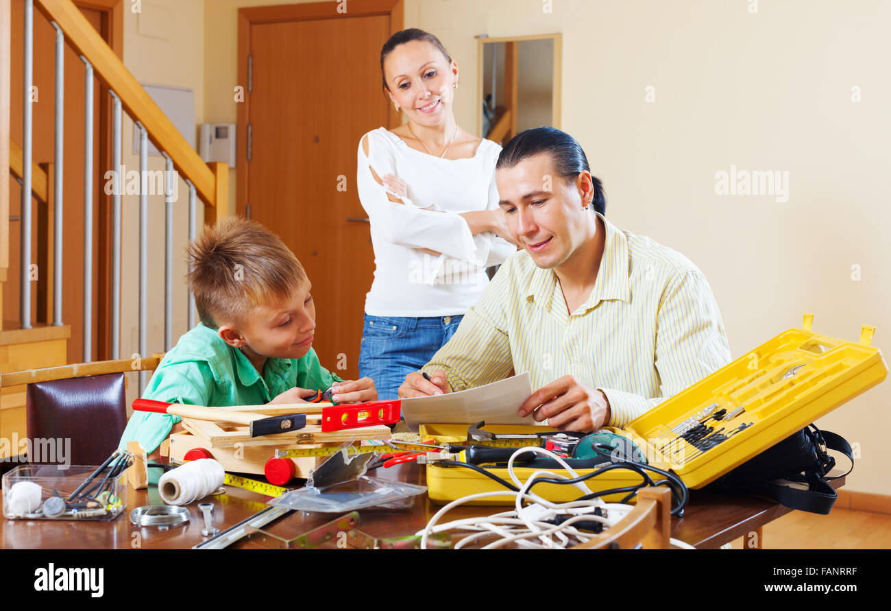 Man with son doing something with the working tool,  woman watching them in home Stock Photo