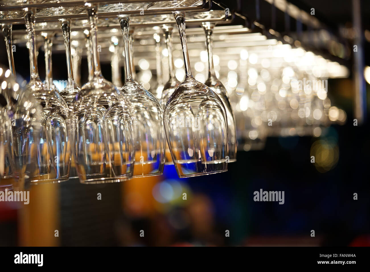 Empty wine glasses hanging on bar rack with bokeh background. Modern restaurant, kitchen utensils, or romantic dinner concept Stock Photo