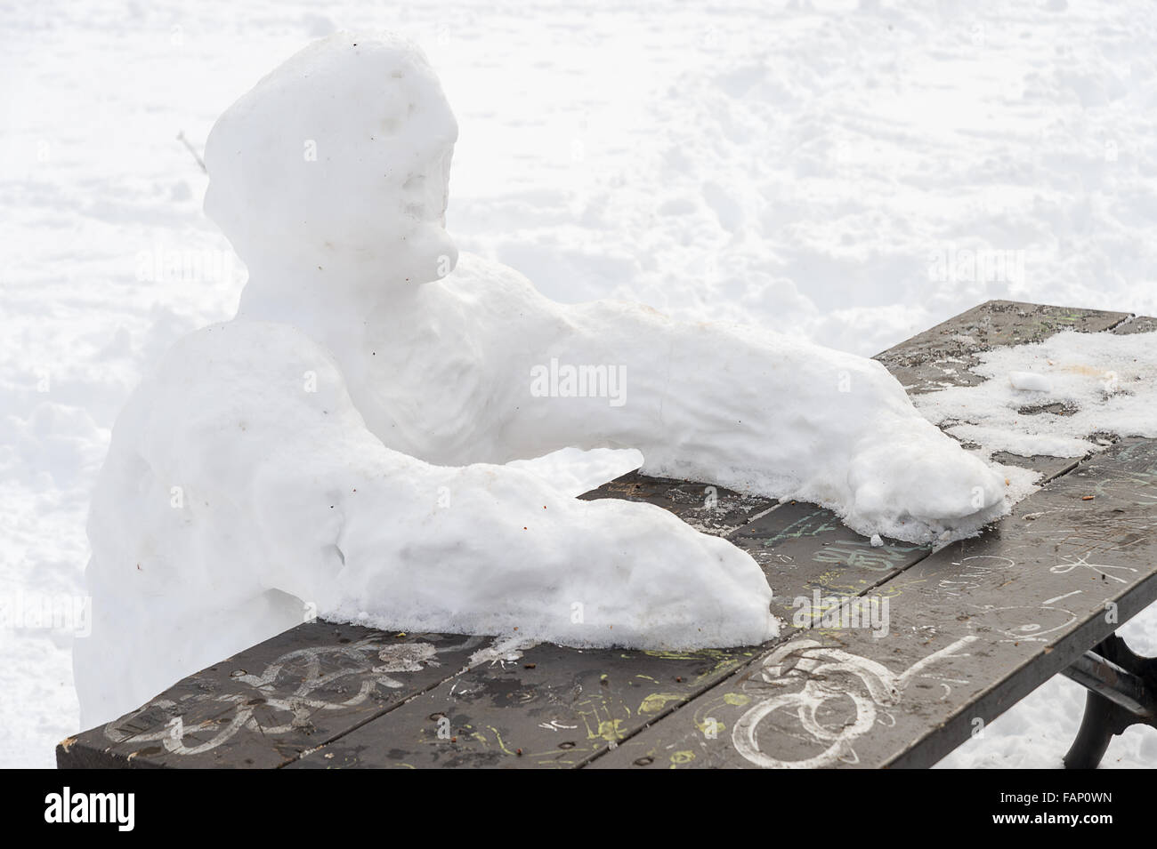 Lonely snow man sitting at picnic table in winter Stock Photo